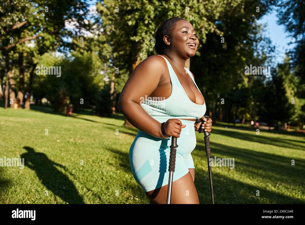 Eine Afroamerikanerin in einem blauen Badeanzug genießt einen sonnigen Tag im Freien, während sie Wanderstöcke hält Stockfoto