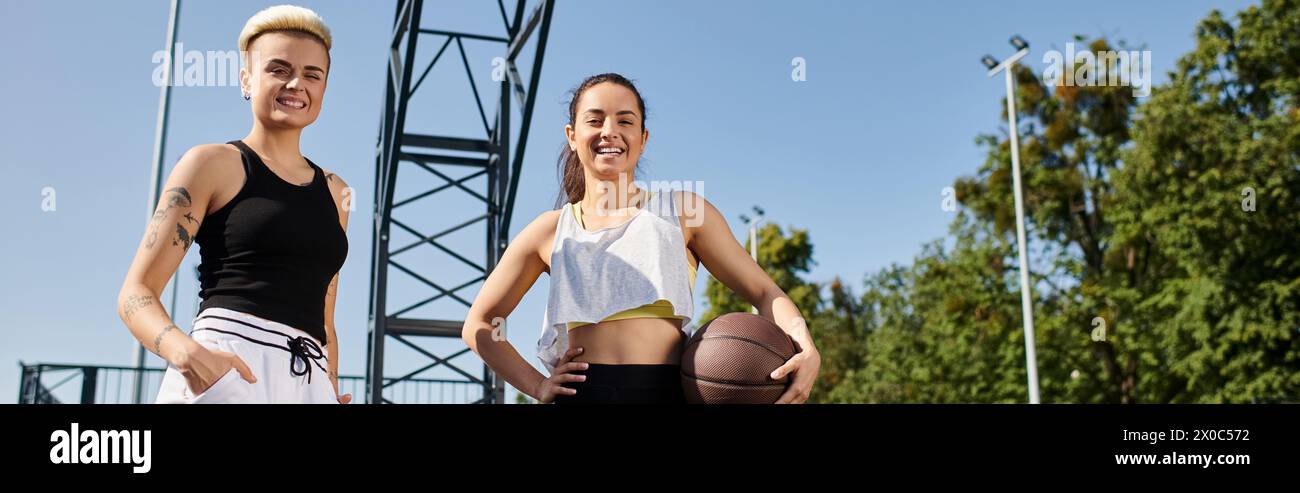 Zwei junge Frauen stehen Seite an Seite, halten einen Basketball und genießen einen sonnigen Tag im Freien. Stockfoto