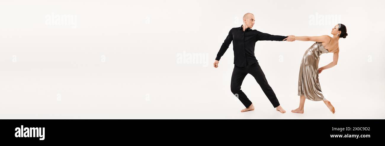 Junger Mann in Schwarz und Frau in silbernem Kleid tanzt fröhlich zusammen und zeigt akrobatische Elemente in einem Studio, das auf weißem Hintergrund gedreht wurde. Stockfoto