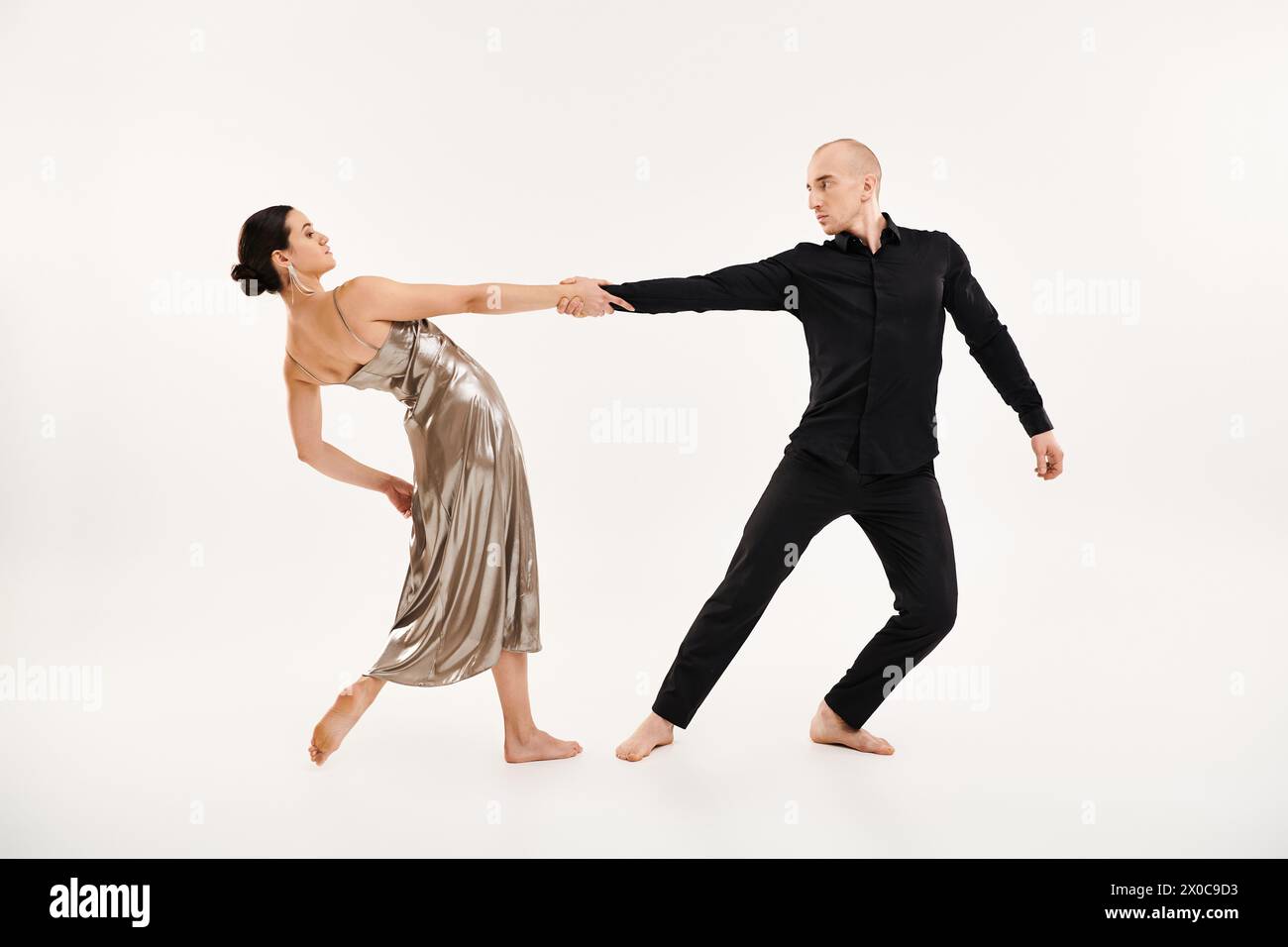 Ein junger Mann in Schwarz und eine junge Frau in einem glänzenden silbernen Kleid mit akrobatischen Tanzbewegungen in einem Studio vor weißem Hintergrund. Stockfoto