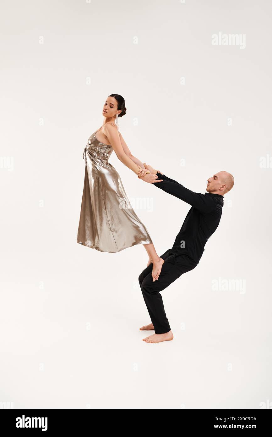 Ein junger Mann in Schwarz und eine Frau in einem silbernen Kleid führen gemeinsam akrobatische Tanzschritte vor weißem Studio-Hintergrund auf. Stockfoto