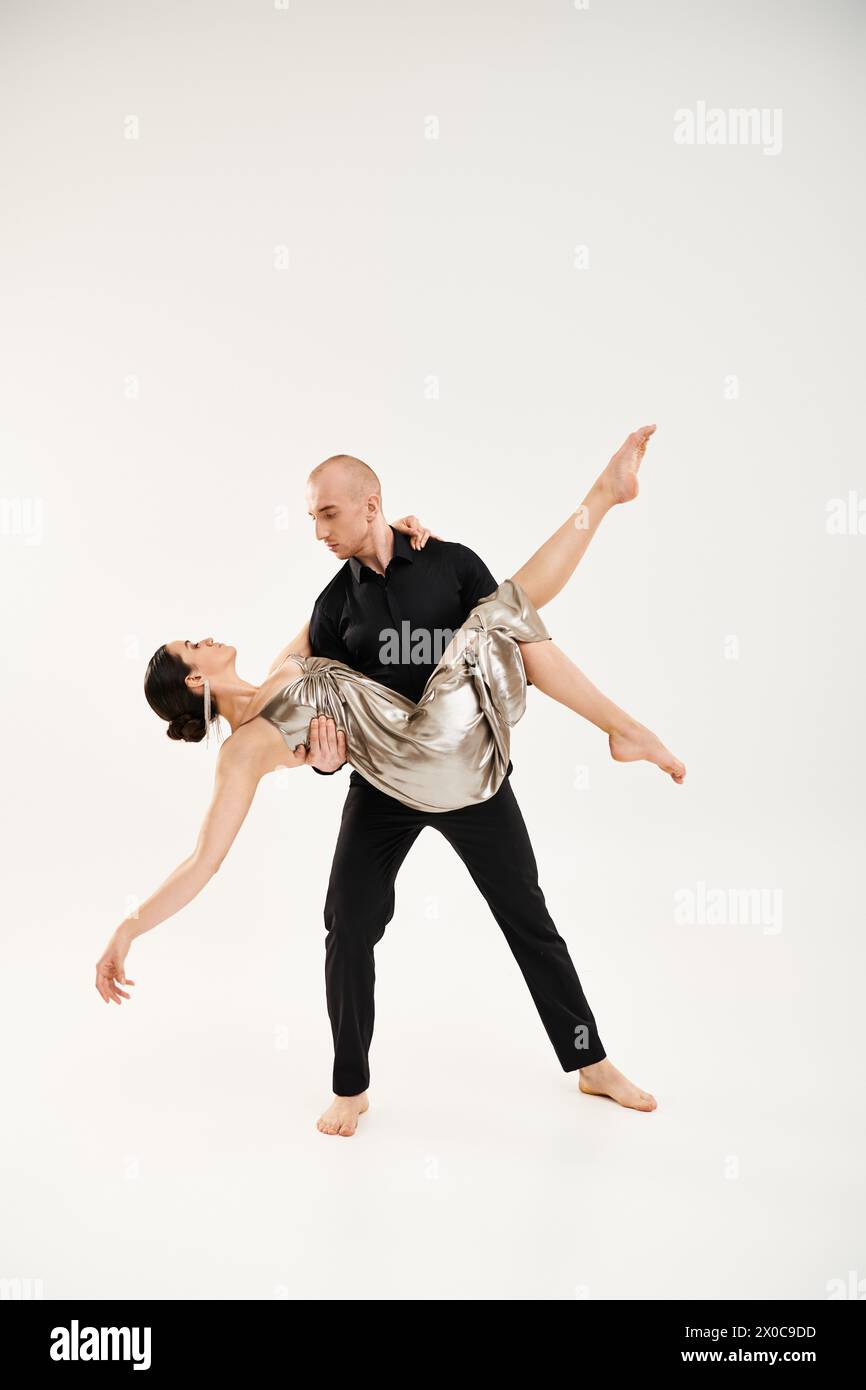 Ein junger Mann in Schwarz und eine junge Frau in einem silbernen, glänzenden Kleid tanzen zusammen und spielen akrobatische Elemente in einem Studio-Setting vor weißem Hintergrund Stockfoto