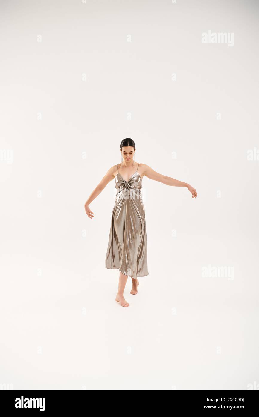 Eine junge Frau tanzt elegant in einem fließenden silbernen Kleid. Stockfoto