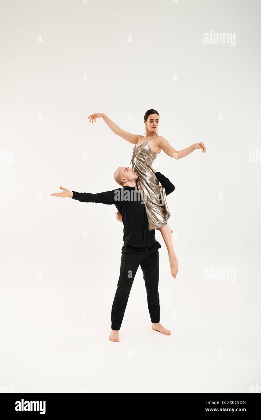 Ein junger Mann in Schwarz trägt eine junge Frau in einem Kleid, während er anmutig tanzt und akrobatische Elemente zeigt. Stockfoto