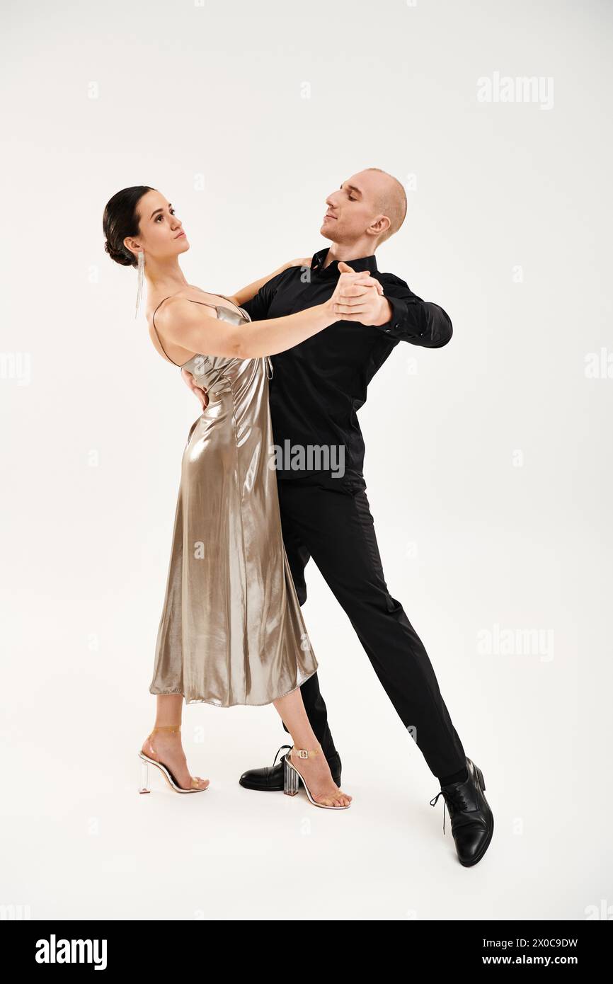 Ein junger Mann in Schwarz und eine junge Frau in einem Kleid führen akrobatische Tanzbewegungen zusammen in einem Studio-Setting auf. Stockfoto