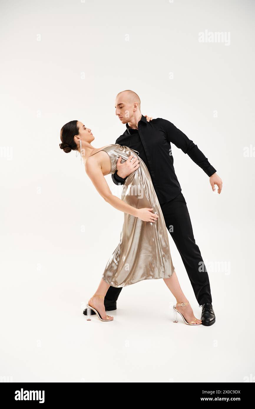Ein junger Mann in Schwarz und eine junge Frau in einem glänzenden Kleid führen akrobatische Tanzschritte zusammen in einem Studio-Setting vor weißem Hintergrund auf. Stockfoto
