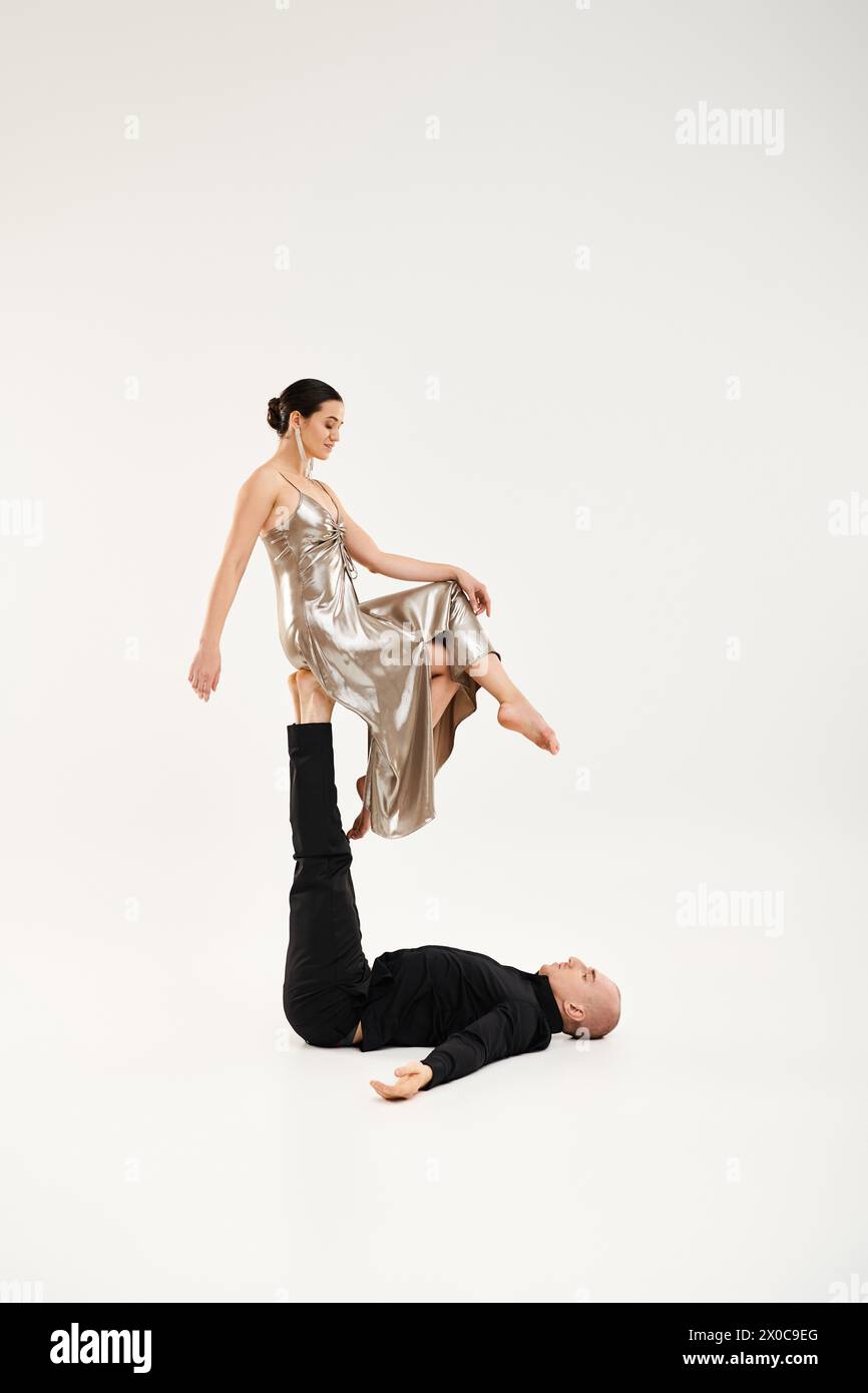 Ein junger Mann in Schwarz und eine junge Frau in einem glänzenden Kleid, die eine akrobatische Tanzroutine in einem Studio vor weißem Hintergrund aufführt. Stockfoto