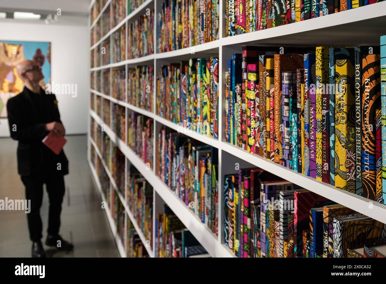 LONDON, VEREINIGTES KÖNIGREICH - 11. APRIL 2024: ein Mitarbeiter sieht sich eine neue Großinstallation mit dem Titel „war Library“ (2024) an, die aus 5.000 Büchern besteht, die in holländischem Wachsdruck gebunden sind und Konflikte und Friedensverträge darstellen, während eines Fotoaufrufs für Yinka Shonibares Ausstellung „Suspended States“ am 11. April 2024 im Londoner Serpentine South in Großbritannien. Die erste Einzelausstellung von Shonibares Werk in einer öffentlichen Londoner Institution seit über 20 Jahren beschäftigt sich mit zentralen Themen des Vermächtnisses der Kolonialmacht, der Zuflucht- und Schutzorte sowie den ökologischen Auswirkungen der Kolonialisierung, dem europäischen Erbe Stockfoto