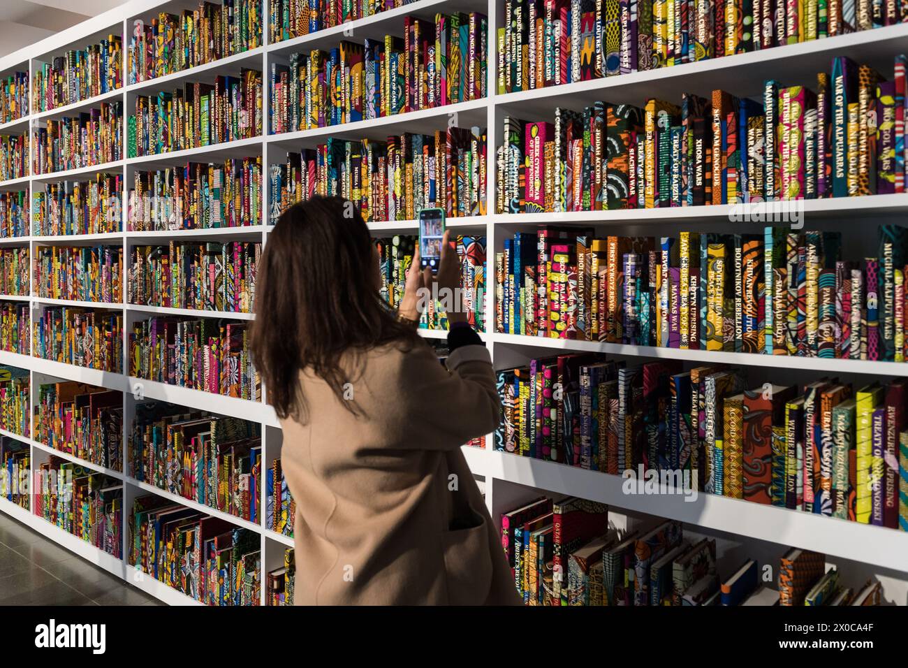 LONDON, VEREINIGTES KÖNIGREICH - 11. APRIL 2024: ein Besucher fotografiert eine neue großformatige Installation mit dem Titel „war Library“ (2024), die aus 5.000 Büchern besteht, die in holländischem Wachsdruck gebunden sind und Konflikte und Friedensverträge darstellen, während eines Fotoaufrufs für Yinka Shonibares Ausstellung „Suspended States“ am 11. April 2024 im Serpentine South in London, Großbritannien. Die erste Einzelausstellung von Shonibares Werk in einer öffentlichen Londoner Institution seit über 20 Jahren beschäftigt sich mit zentralen Themen des Vermächtnisses der Kolonialmacht, der Zuflucht- und Schutzorte sowie den ökologischen Auswirkungen der Kolonisierung, dem europäischen Bein Stockfoto