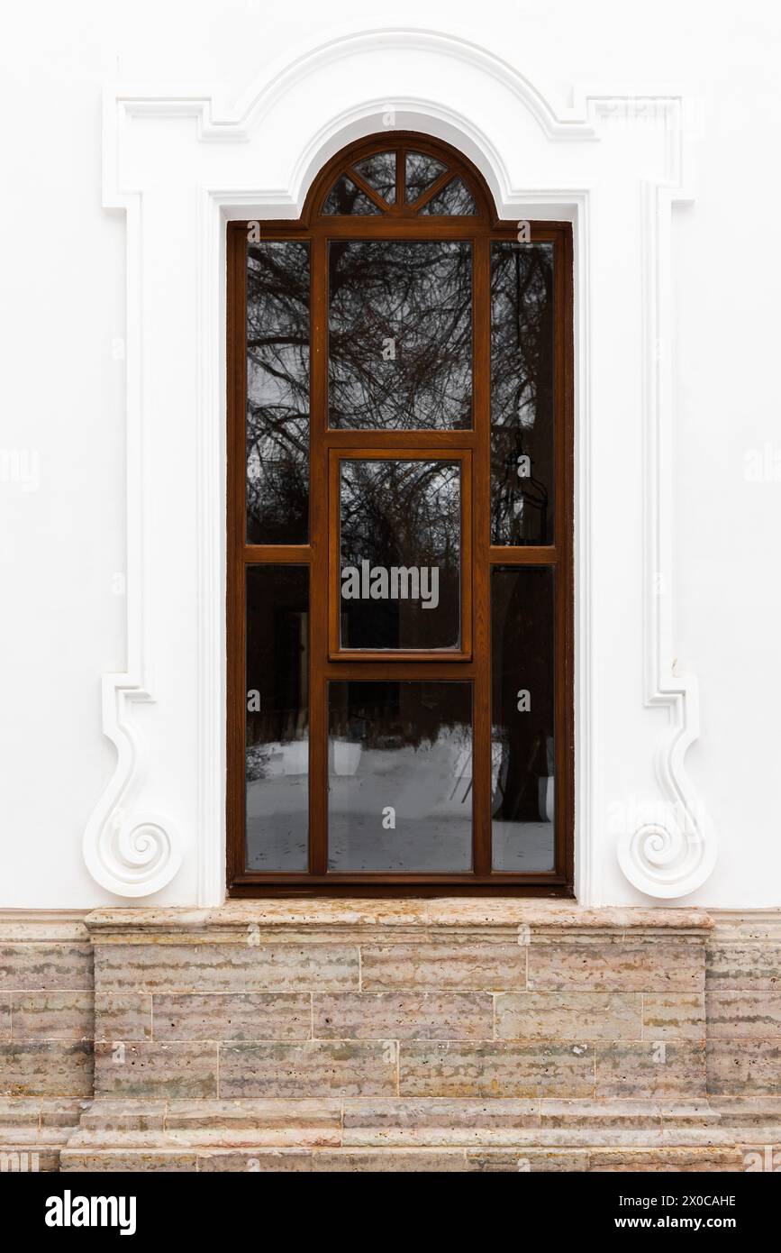 Klassisches Fenster mit Bogen und dekorativen Elementen in weißer Steinwand. Hintergrundfotostruktur Stockfoto