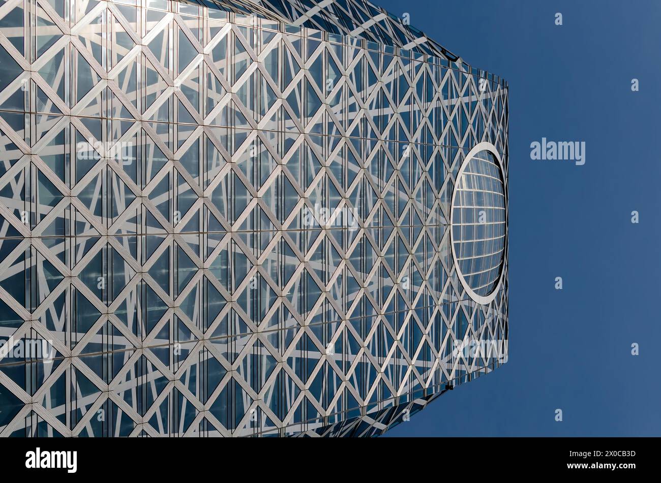 Ein hohes Gebäude mit einem großen runden Fenster auf der Oberseite. Das Gebäude ist aus Glas und hat ein modernes Design. Der Himmel ist klar und blau, und die Sonne Stockfoto