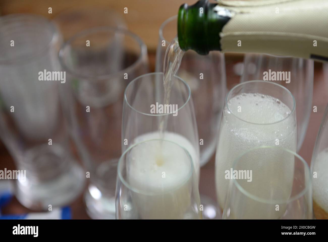Eine Flasche Champagner wird in eine Reihe von Weingläsern gegossen. Das Konzept des Feierns und Genusses Stockfoto