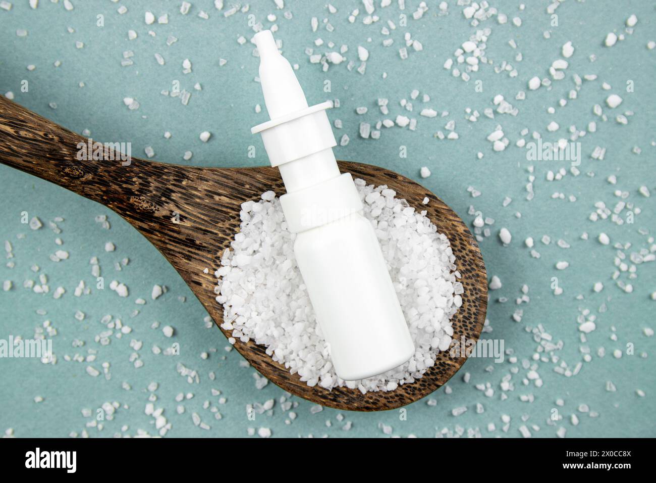 Hausgemachte salzige Nasensprayflasche auf verstreuten Meersalzkörnern und Holzlöffel auf blauem Hintergrund, Studioaufnahme. Stockfoto