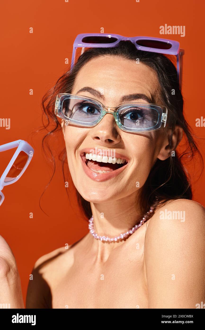 Eine modische Frau, die eine Brille auf orangefarbenem Hintergrund trägt. Stockfoto