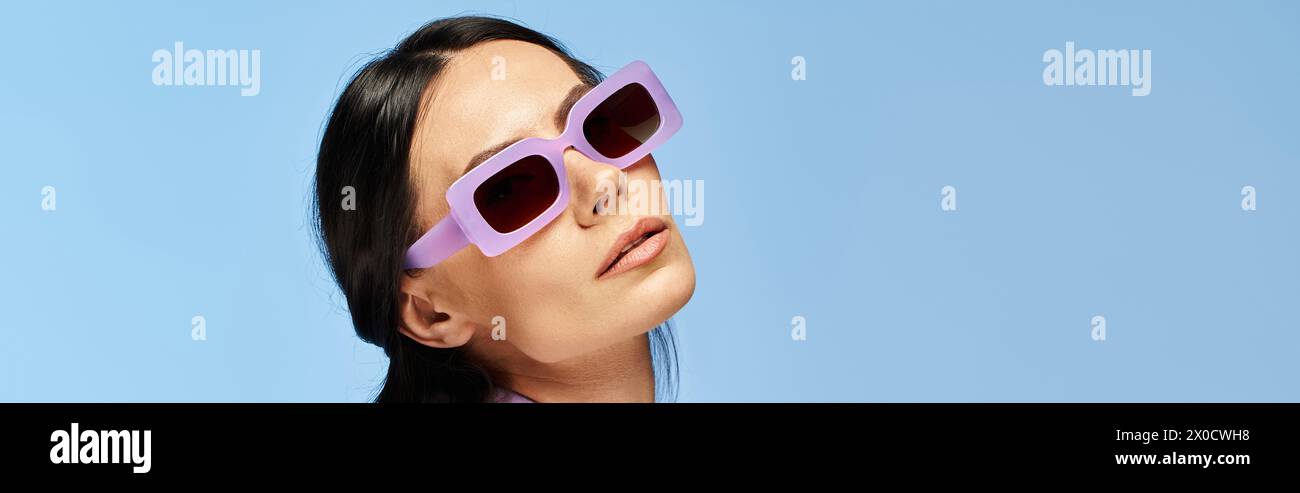 Eine stilvolle Frau mit Sonnenbrille blickt in den Himmel vor blauem Studio-Hintergrund. Stockfoto