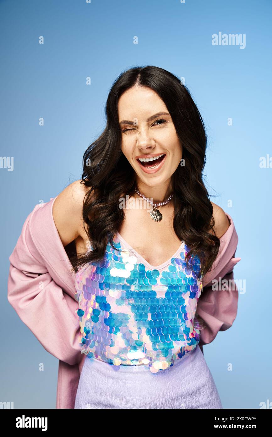 Eine atemberaubende Frau mit einem lila Oberteil lächelt fröhlich in einem Studio mit einem leuchtend blauen Hintergrund. Stockfoto
