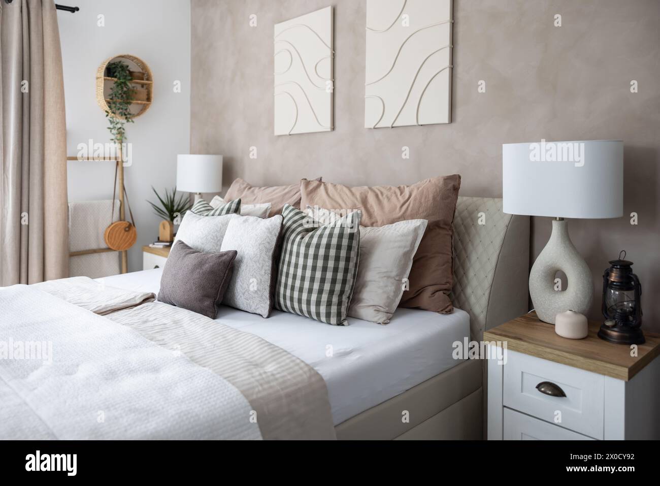 Moderne Innenausstattung des Schlafzimmers, weiße Decke, viele Kissen und stilvolle Nachtlampen. Stockfoto