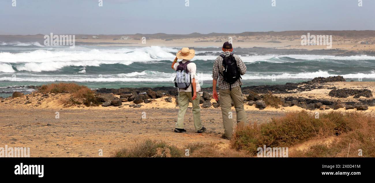 Reife Paare spazieren entlang der Küste in Punta Tostón, El Cotillo, Fuerteventura, Kanarischen Inseln mit rauen Atlantikwellen. Vom Februar 2024 Stockfoto