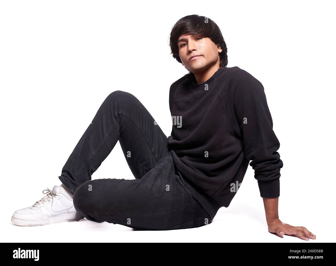 Ein Mann in schwarzem Sweatshirt und schwarzer Hose sitzt auf dem Boden. Er trägt weiße Schuhe Stockfoto