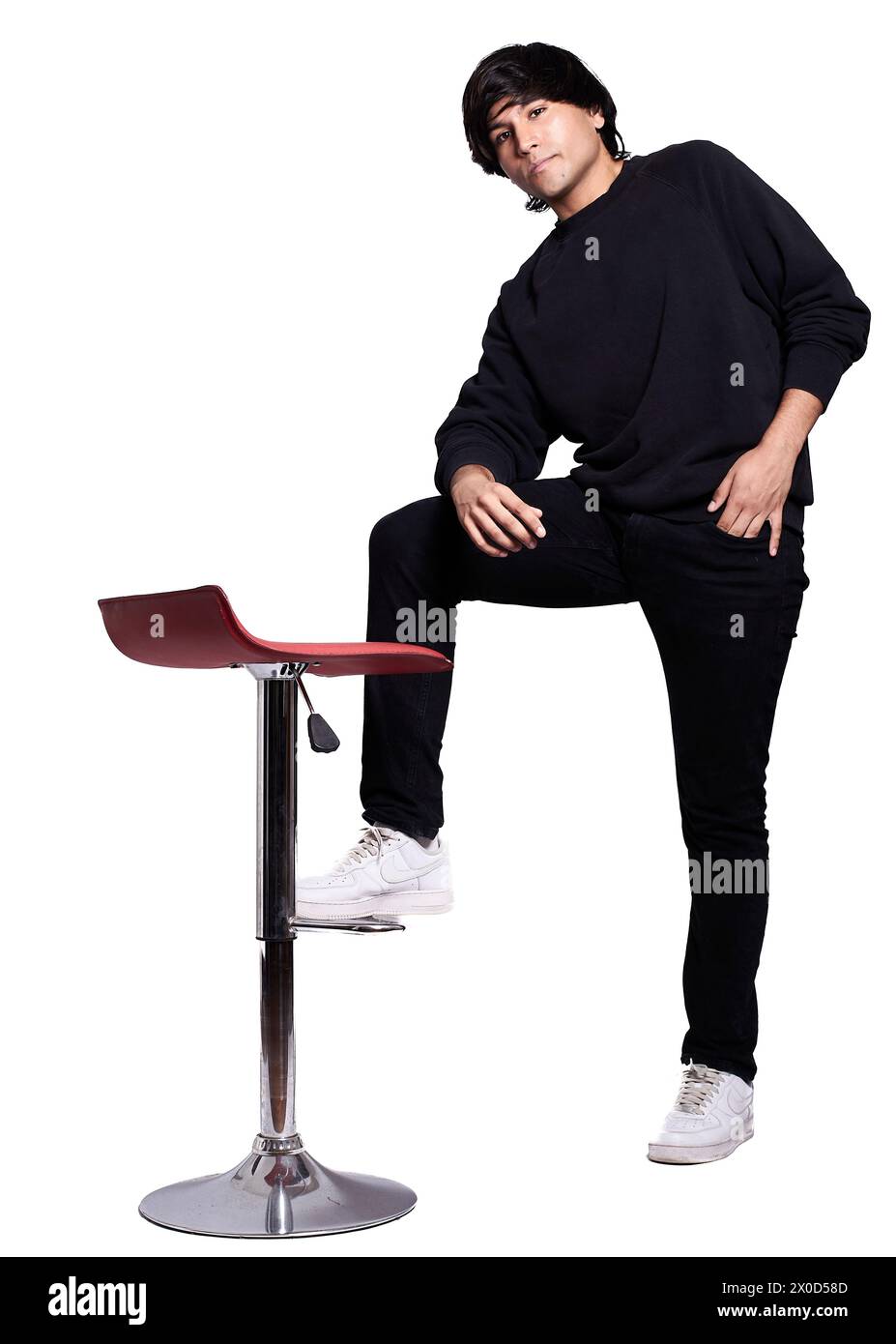 Ein Mann in einem schwarzen Sweatshirt sitzt auf einem roten Hocker. Er trägt weiße Turnschuhe und hat seine Hände in der Tasche Stockfoto