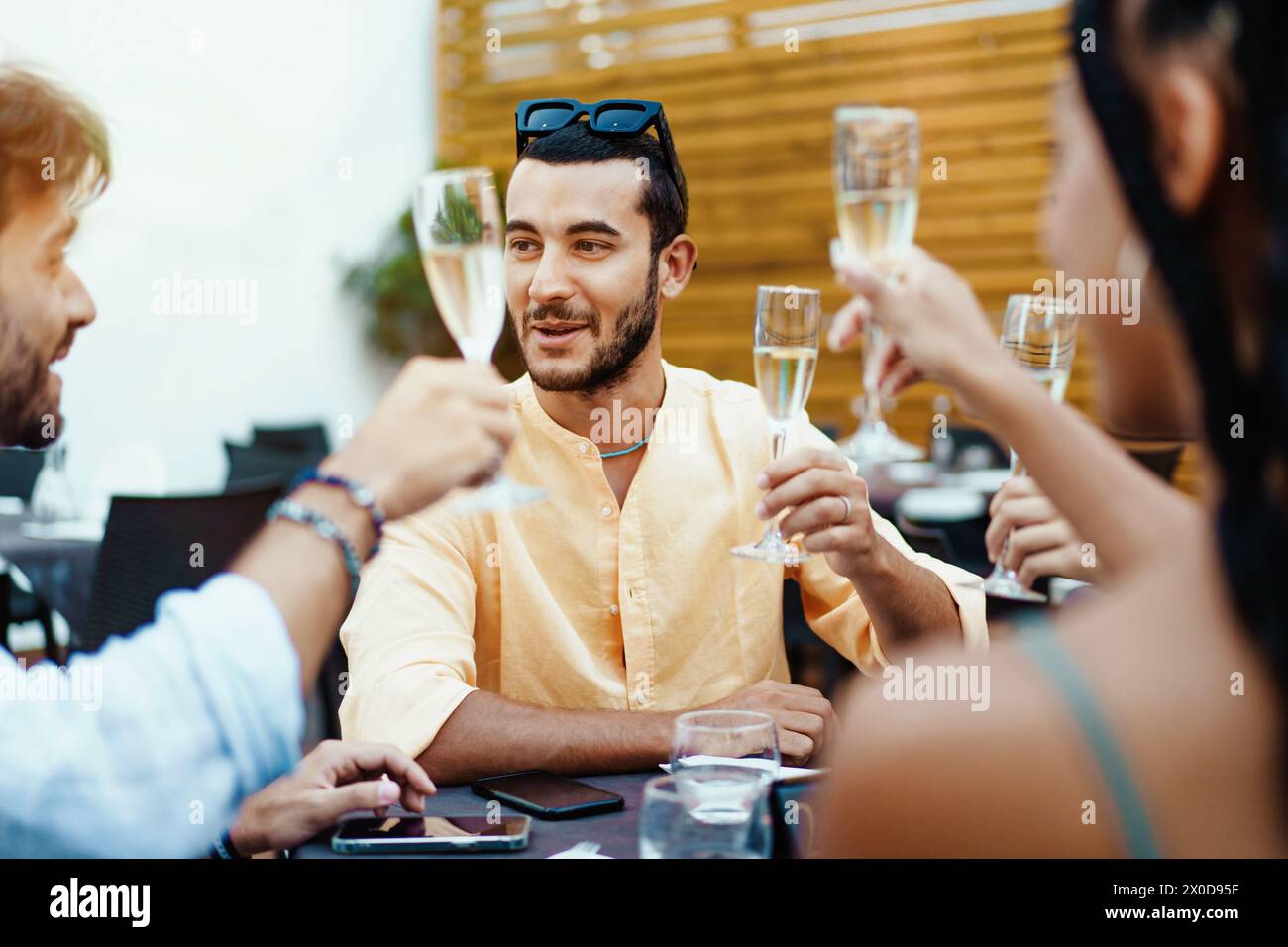 Eine fröhliche Gruppe von Freunden, die ihre Sektgläser zum Toast hochheben - zwangloses Abendessen im Freien, das die Freude an der Zweisamkeit verkörpert. Stockfoto