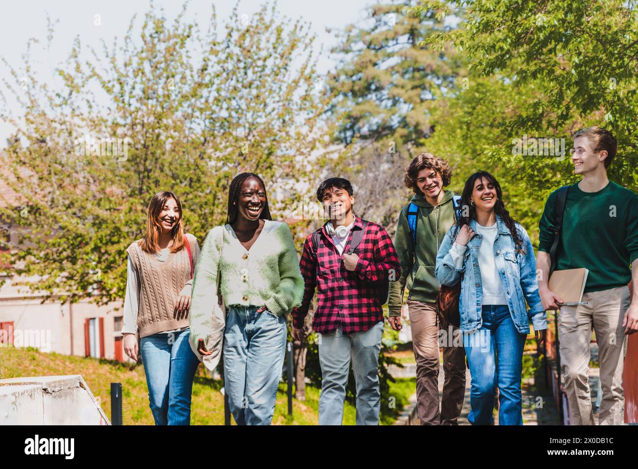 Eine vielfältige Gruppe von Universitätsstudenten genießt einen sonnigen Tag auf dem Campus - Freunde laufen und lachen zusammen, teilen einen Moment echter Freundschaft und Stockfoto