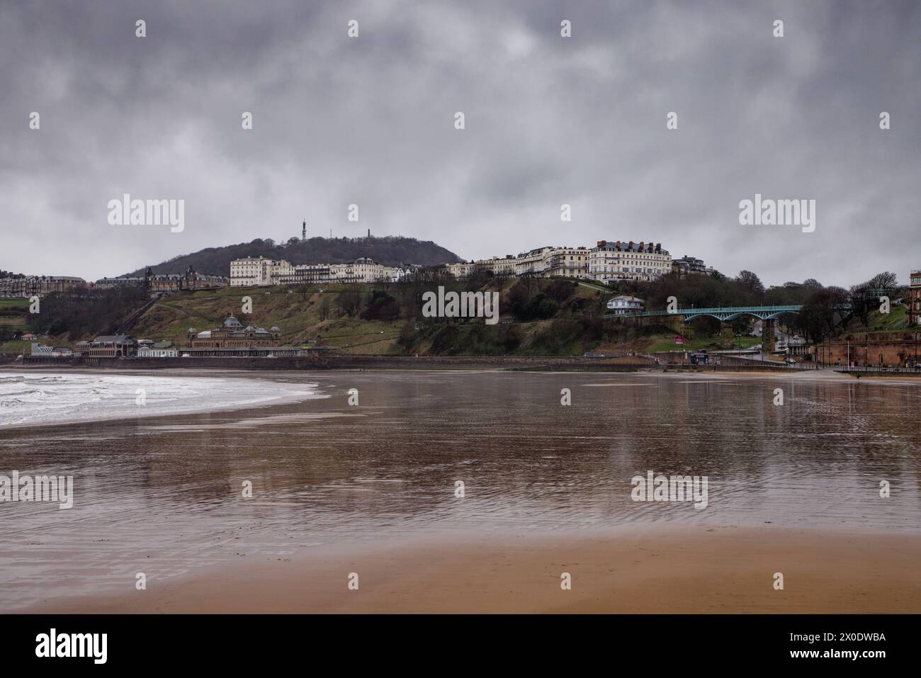 Scarborough, North Yorkshire, England, ein Sandstrand bei Ebbe mit einem Resort an Klippen und einem stimmungsvollen Regenhimmel. Stockfoto