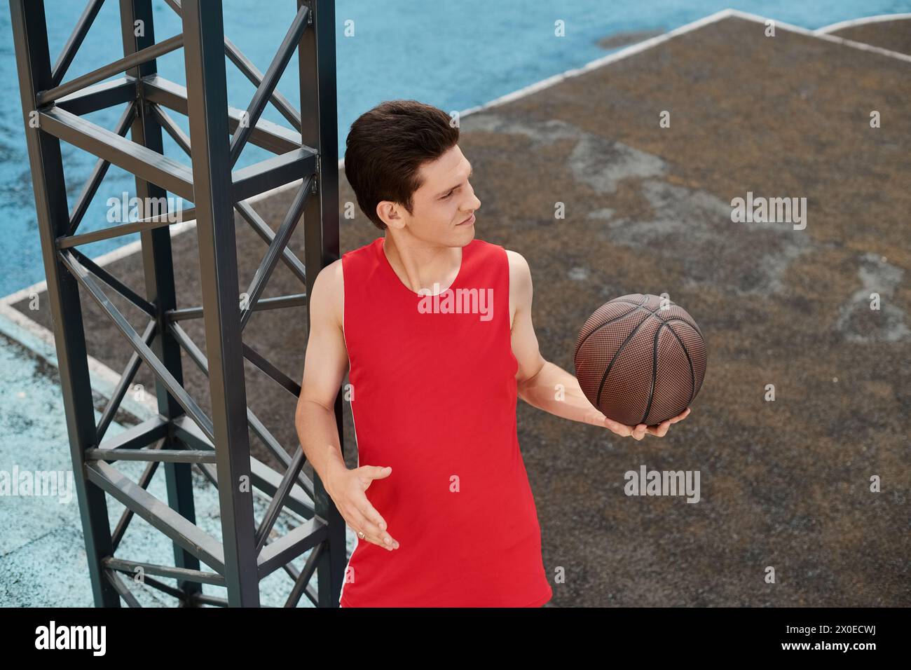 Ein junger Mann in rot gekleidet, der an einem Sommertag im Freien seine Basketballfähigkeiten zeigt. Stockfoto