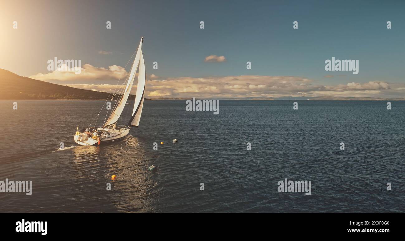 Sonne über Segelregatta auf Luxusyachten aus der Luft. Filmisches Seeblick am sonnigen Sommertag. Majestätische Segelboote fahren an der Meeresbucht im Hafen von Brodick, Arran Island, Schottland. Panorama-Drohne aufgenommen Stockfoto