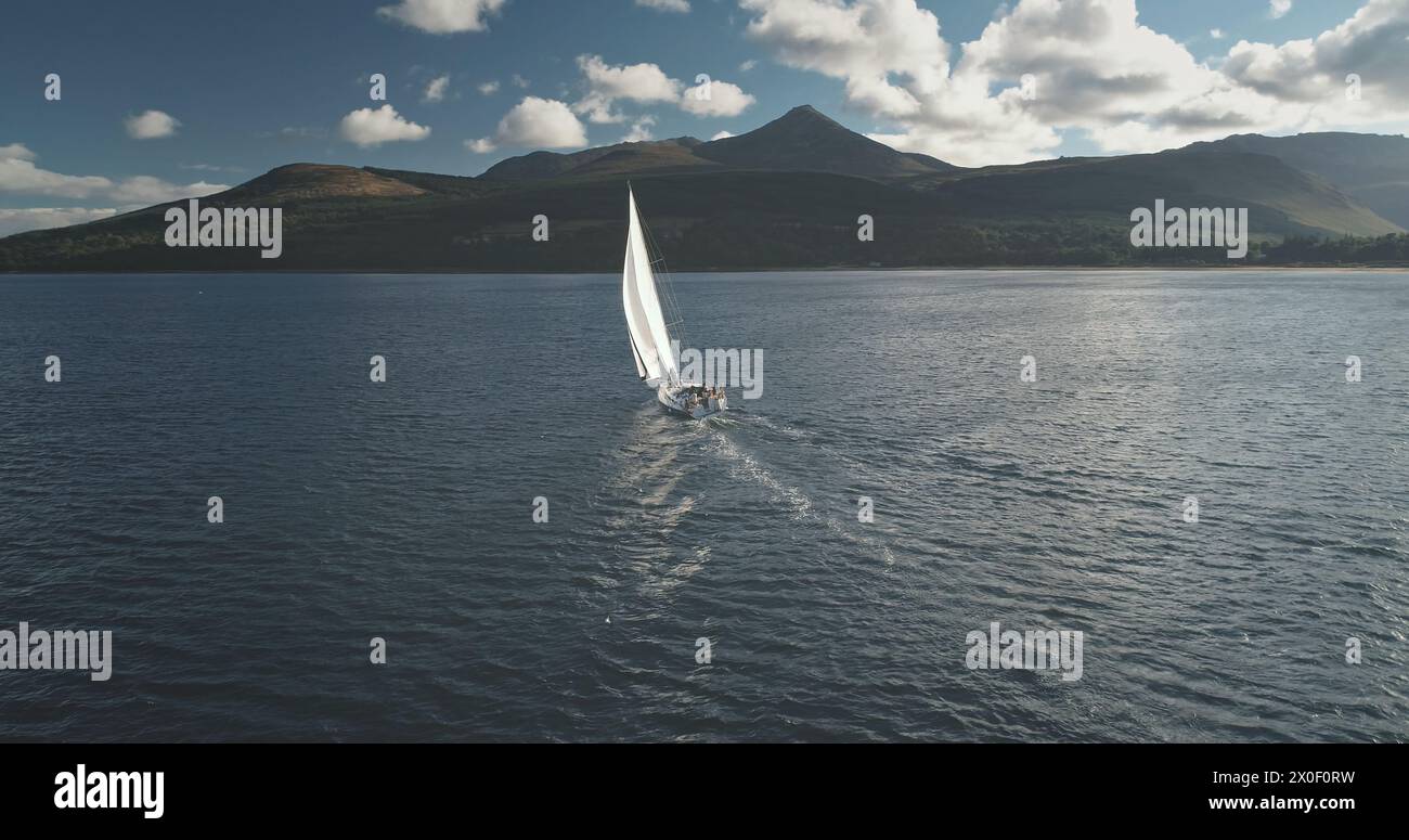 Zeitlupe der Yacht, Wind weht, um an der Meeresbucht zu segeln. Berginsel Arran, Schottland, Europa. Am Brodick Gulf gibt es keine Naturlandschaft. Luxuriöse Bootstour auf einem Segelboot. Kinotourismus-Lebensstil Stockfoto