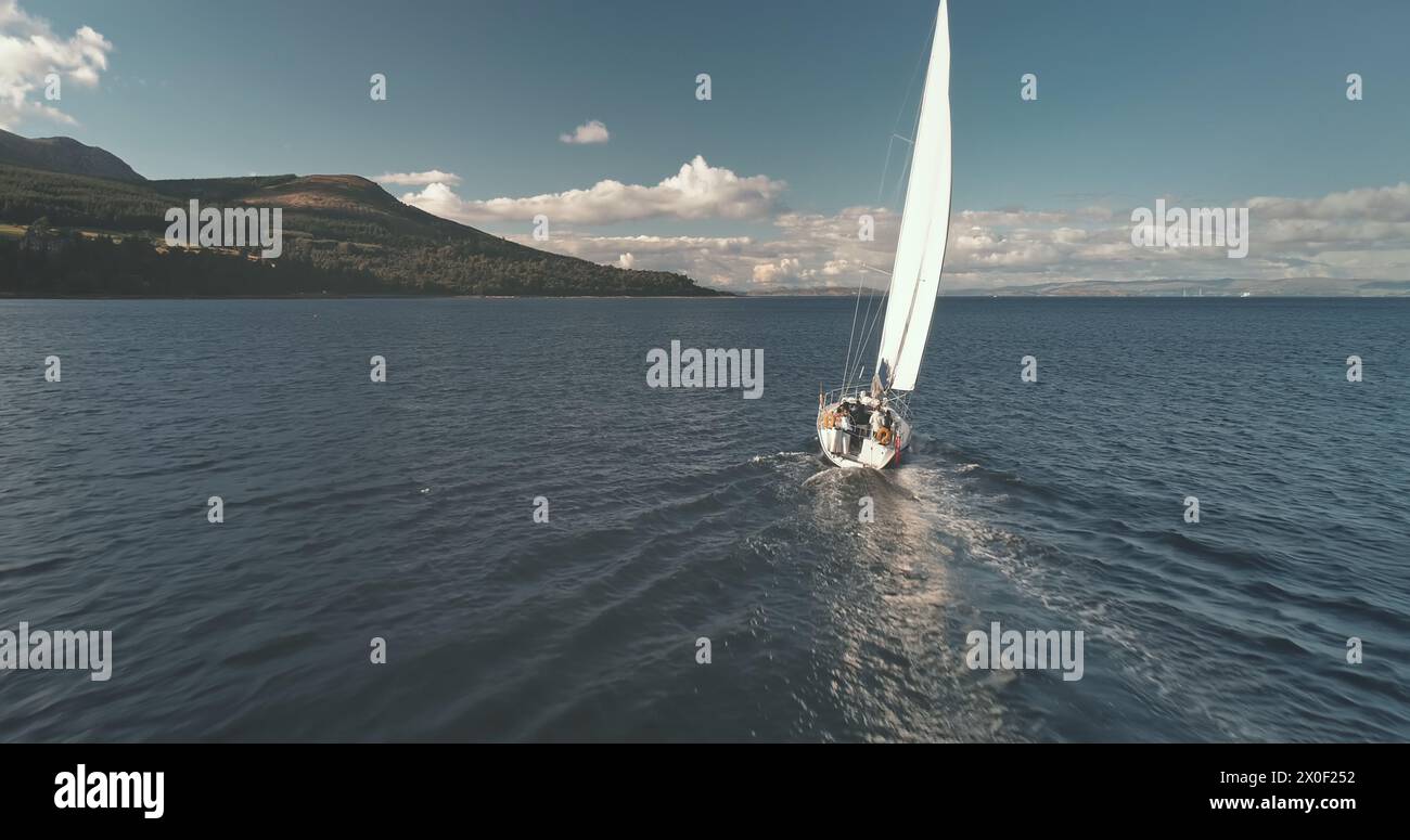 Rennyacht am Golf von Brodick Harbour Aerial. Die bergige Inselküste bietet eine fantastische Meereslandschaft. Luxusschiff an der Küste. Segelboot Reflect am Brodick Pier, Arran isle, Schottland, Europa Stockfoto