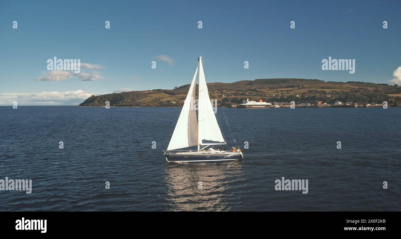 Segelboote fahren auf offener See. Brodick Port, Arran Island, Schottland. Naturlandschaft am Sommertag. Yachting am Frachtterminal auf der Ozeanhafenflugbahn. Regatta auf einer Luxusyacht. Filmdrohnenaufnahme Stockfoto