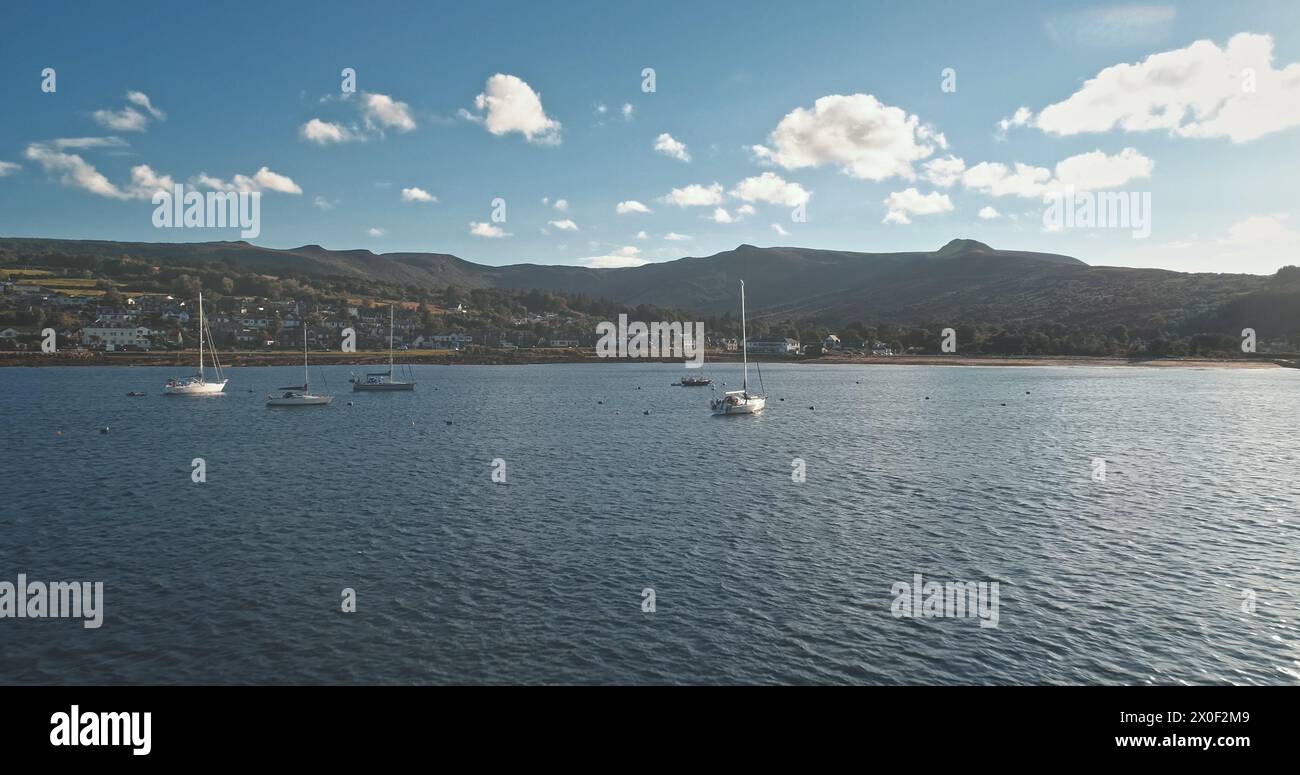 Regatta auf Luxusyachten aus der Luft. Segelboote fahren an der Meeresbucht im Hafen von Brodick, Arran Island, Schottland, Europa. Filmische Meereslandschaft des Sommerurlaubs sonniger Tag. Panorama-Drohne aufgenommen Stockfoto