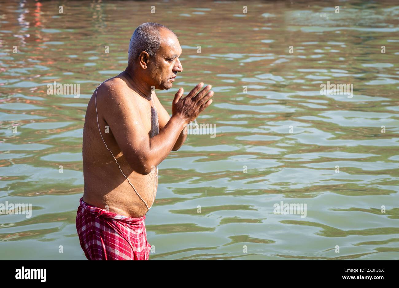 Geweihter betet nach dem Baden in heiligem Flusswasser am Morgen aus flachem Winkel Stockfoto