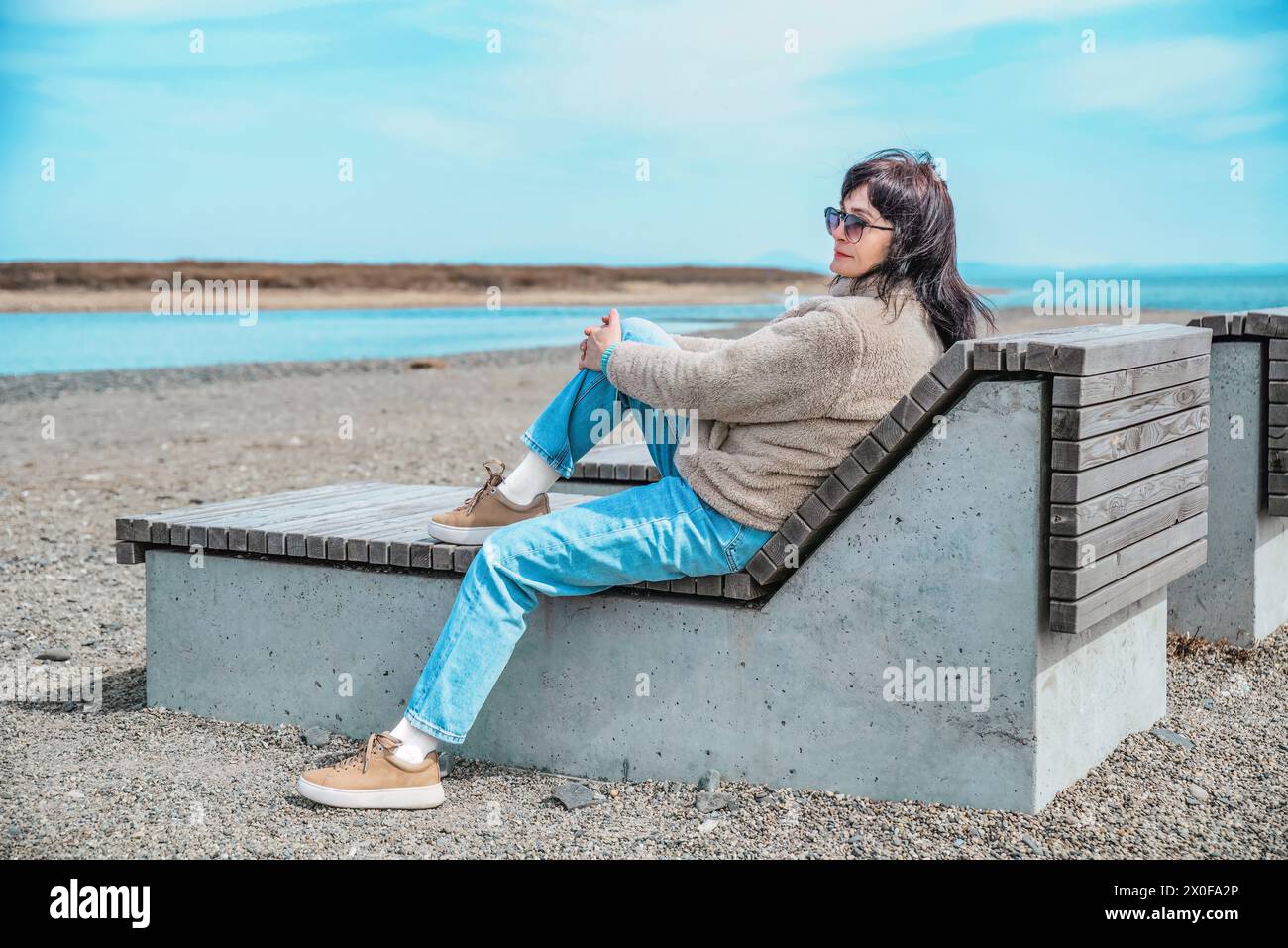 49-jährige Russin, die an einem frühen Frühlingstag auf einer Bank vor dem japanischen Meer sitzt Stockfoto