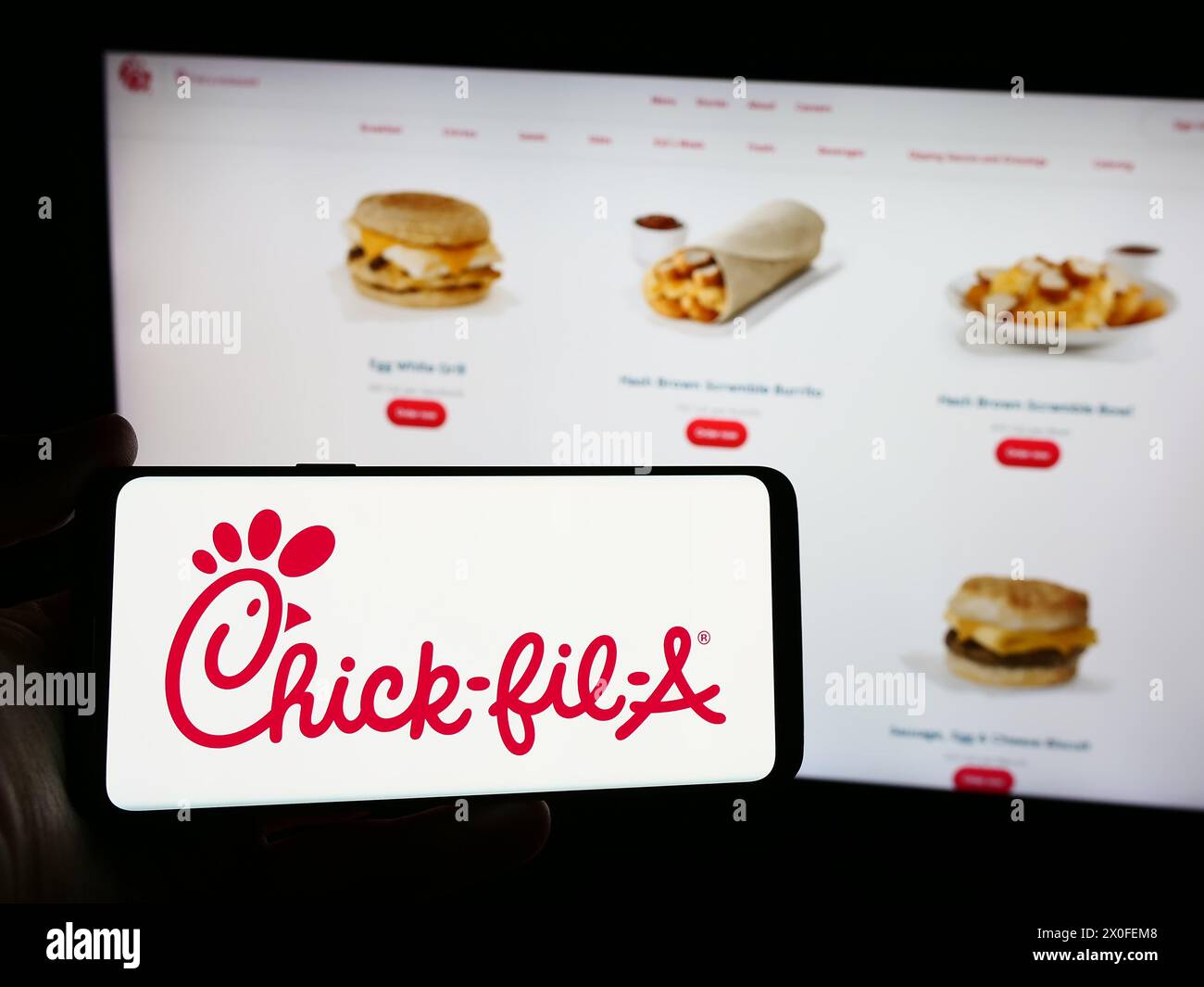 Person mit Smartphone und Logo des US-amerikanischen Fast-Food-Restaurantunternehmens Chick-Fil-A Inc. Vor der Website. Schwerpunkt auf dem Display des Telefons. Stockfoto