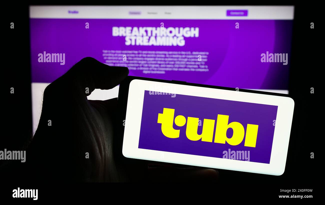 Person, die ein Mobiltelefon mit dem Logo der amerikanischen Streaming-Plattform Tubi Inc. Vor der Business-Webseite hält. Schwerpunkt auf dem Display des Telefons. Stockfoto