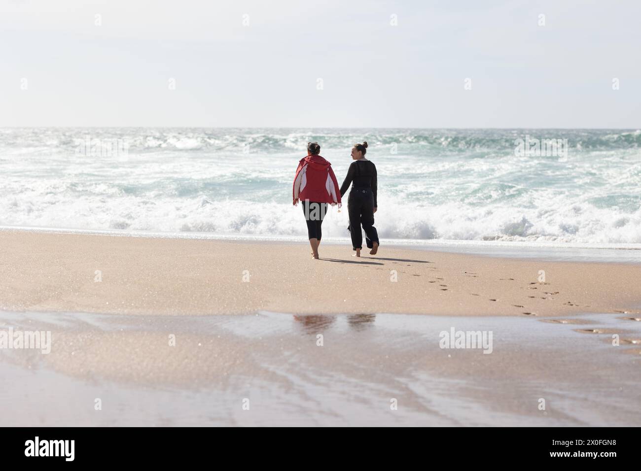 Zwei Freundinnen, die an einem Strand laufen und Hände halten Stockfoto