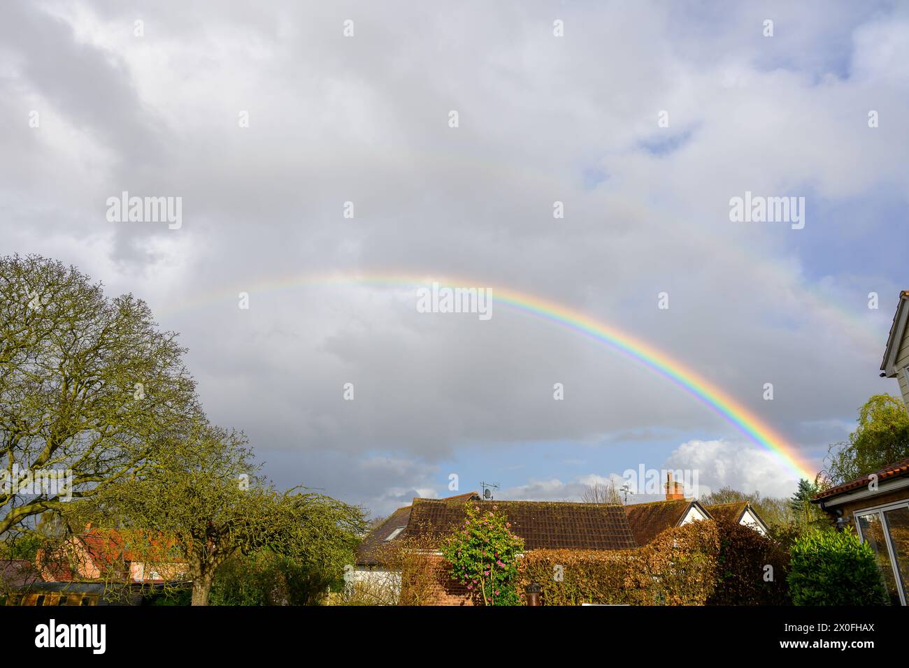 Ein Regenbogen, der sich über die Dächer erhebt, mit den stürmenden grauen Wolken im Hintergrund Stockfoto