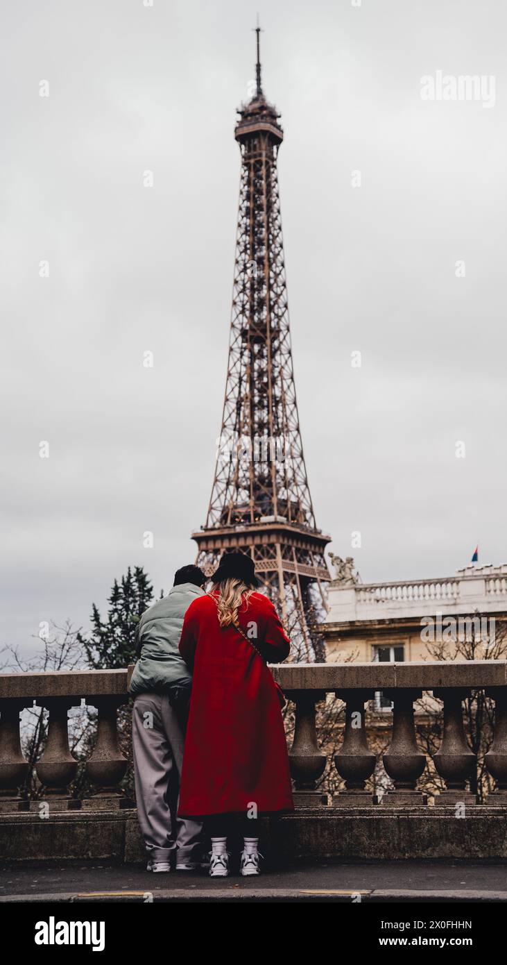 Ein Paar, das den Eiffelturm von einer Straße in Paris aus betrachtet. Frau in rotem Kleid und schwarzem französischem Hut Stockfoto