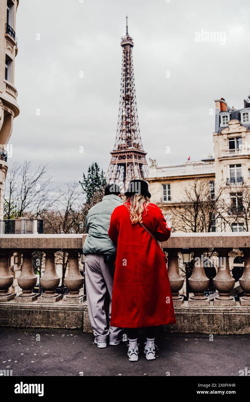 Ein Paar, das den Eiffelturm von einer Straße in Paris aus betrachtet. Frau in rotem Kleid und schwarzem französischem Hut Stockfoto