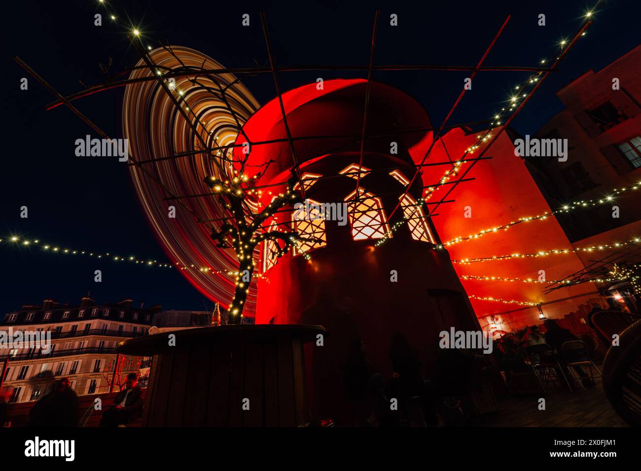 Moulin Rouge bei Nacht mit Lichtern während des französischen Sonnenuntergangs. Drehender moulin in roten Lichtern am Abend. Stockfoto