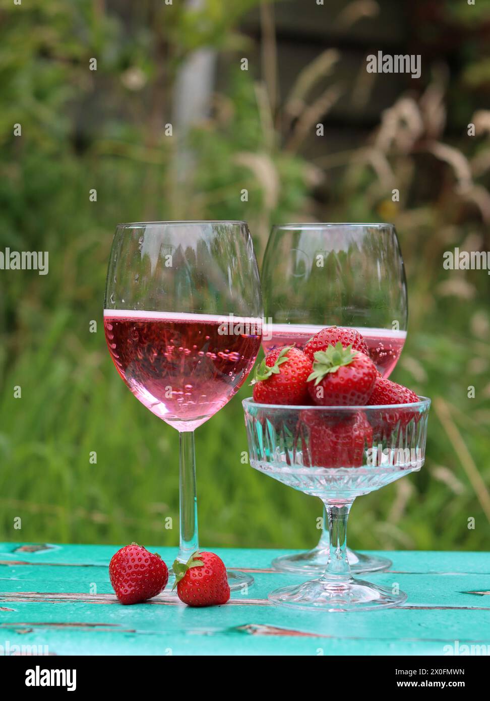 Zwei Gläser Rosenschaum und Erdbeere auf einem Tisch. Romantisches Picknick im Freien. Nahaufnahme des Glasgeschirrs. Getränke und Speisen im Sommer. Stockfoto