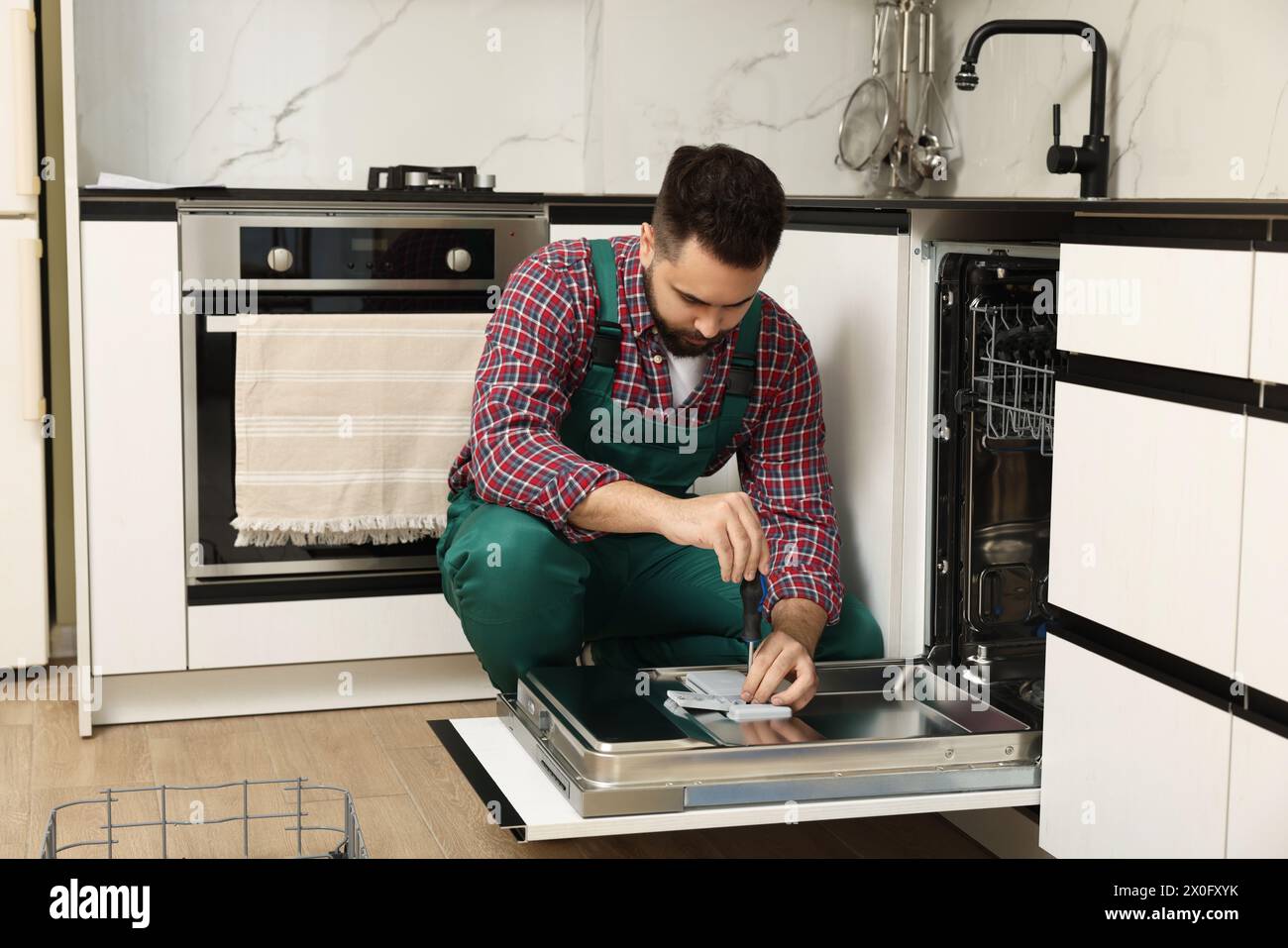 Service repariert Geschirrspüler mit Schraubendreher in der Küche Stockfoto