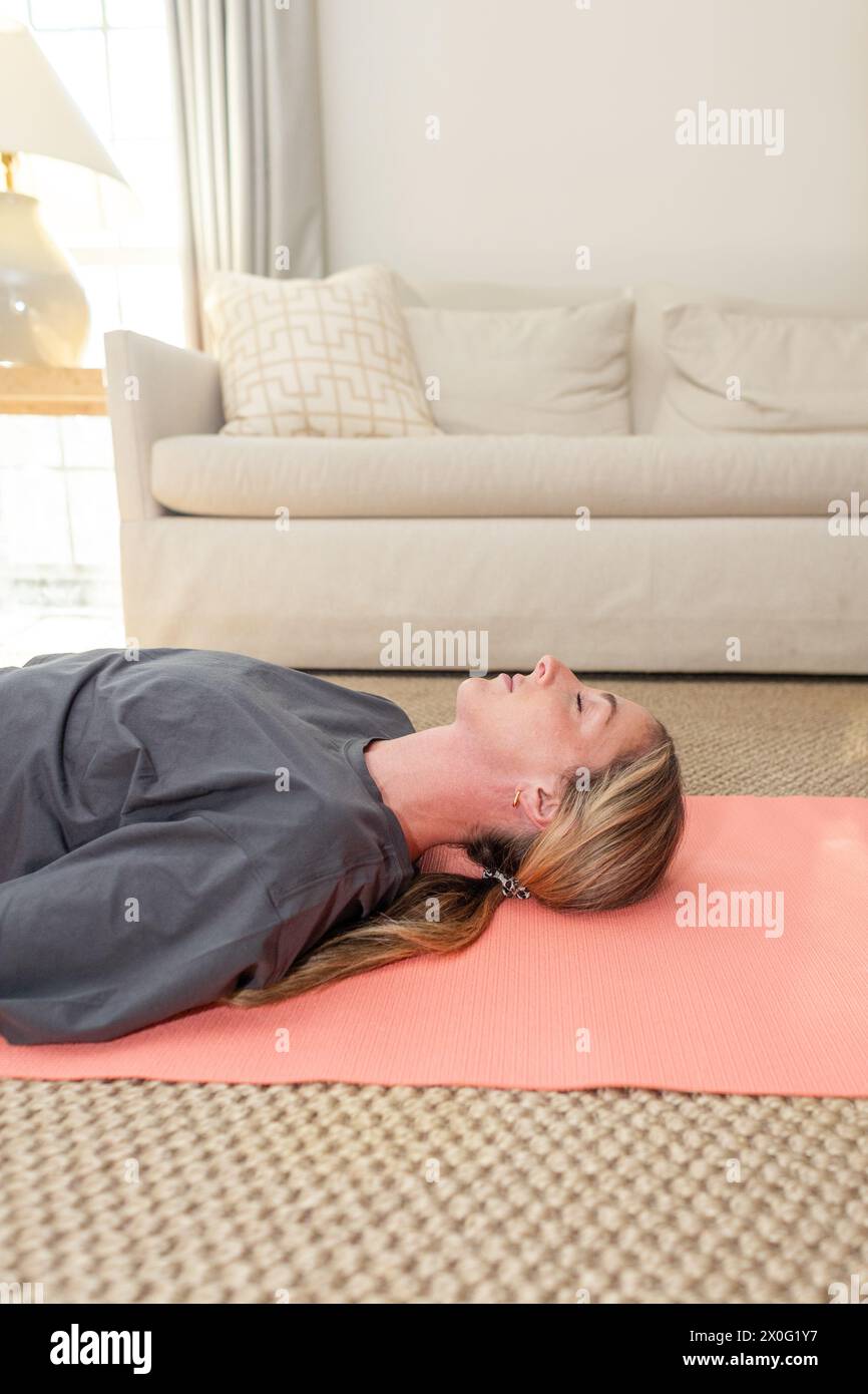 Frau in ruhiger Entspannung posiert auf Yogamatte zu Hause Stockfoto