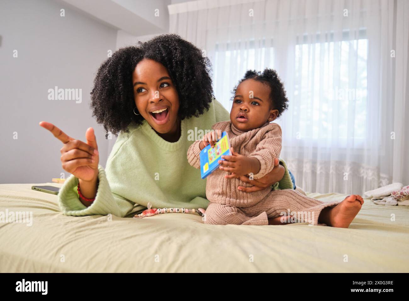 Die kubanische Mutter zeigt ihrer Kleinkind-Tochter etwas im Bett. Stockfoto