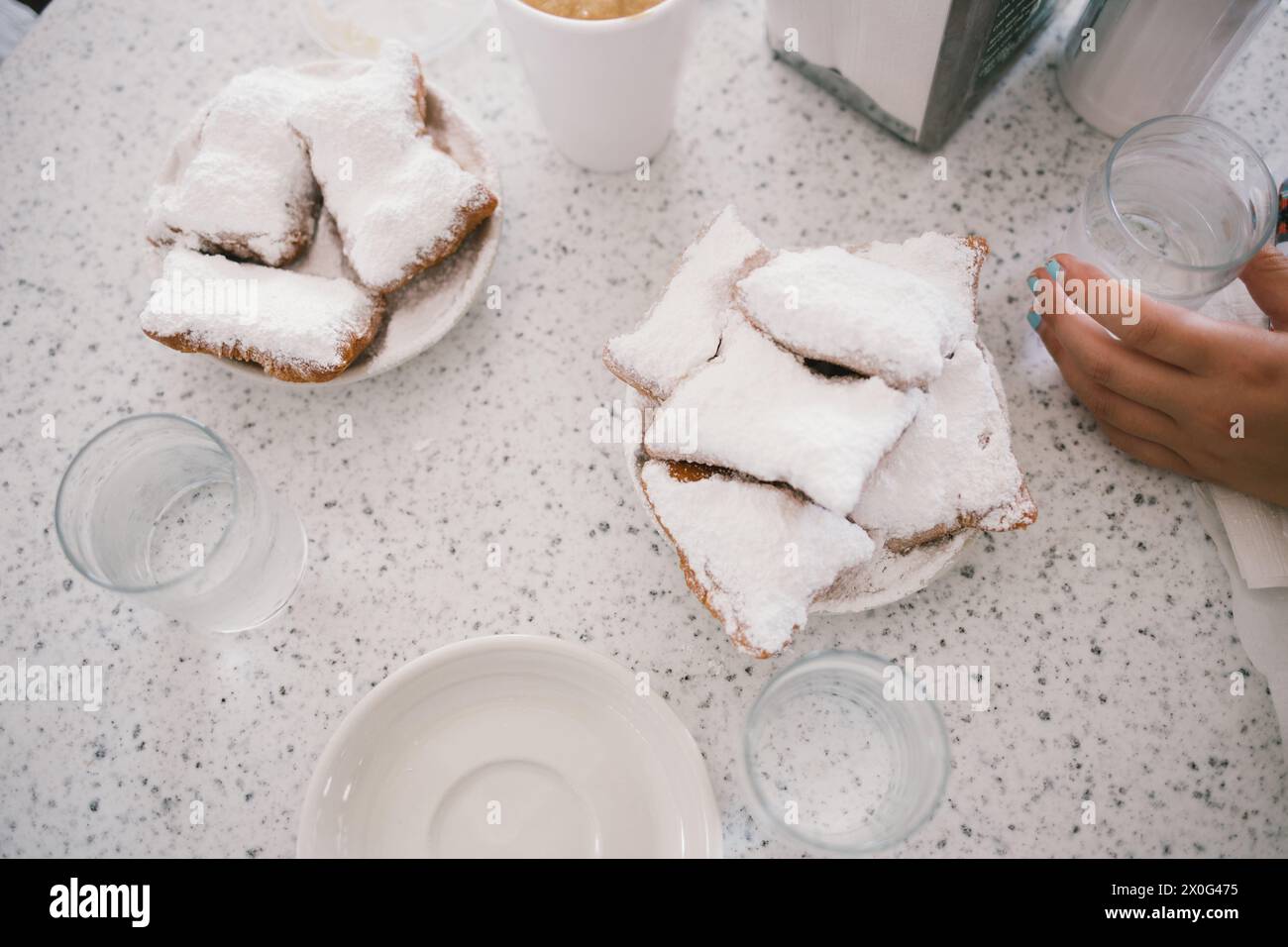 Nahaufnahme frischer Beignets auf dem Kaffeetisch, umgeben von Geschirr und Tassen Stockfoto