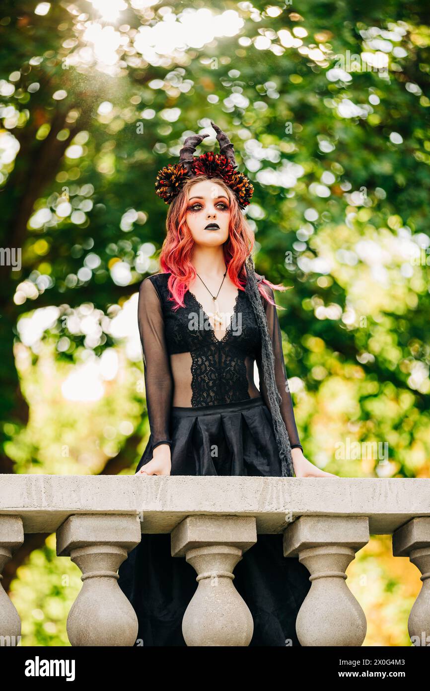Hexenmädchen mit roten Haaren in schwarzem Kleid mit Hörnern Stockfoto