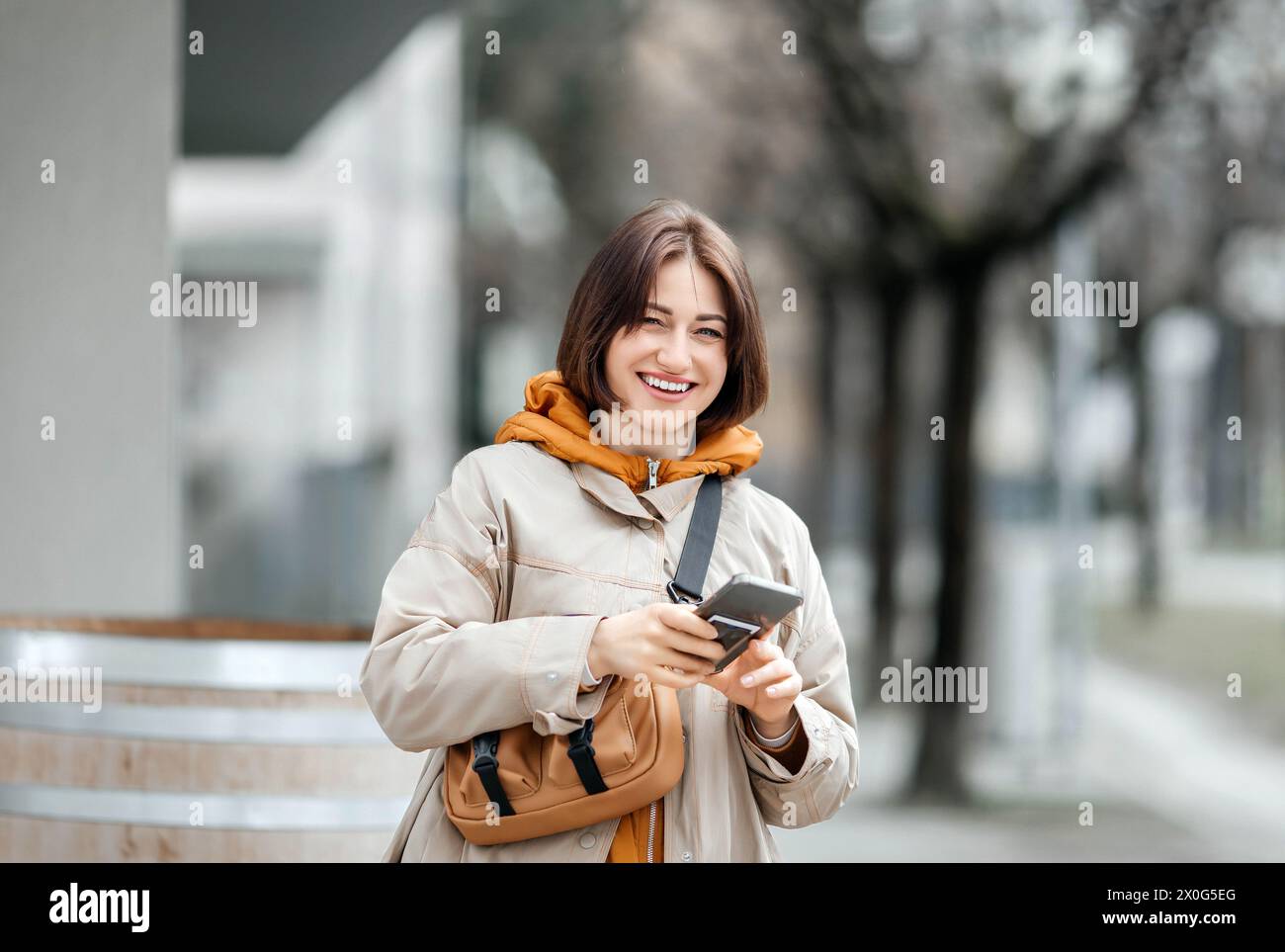 Junge, stilvolle Frau mit Smartphone, das auf der City Street lächelt Stockfoto