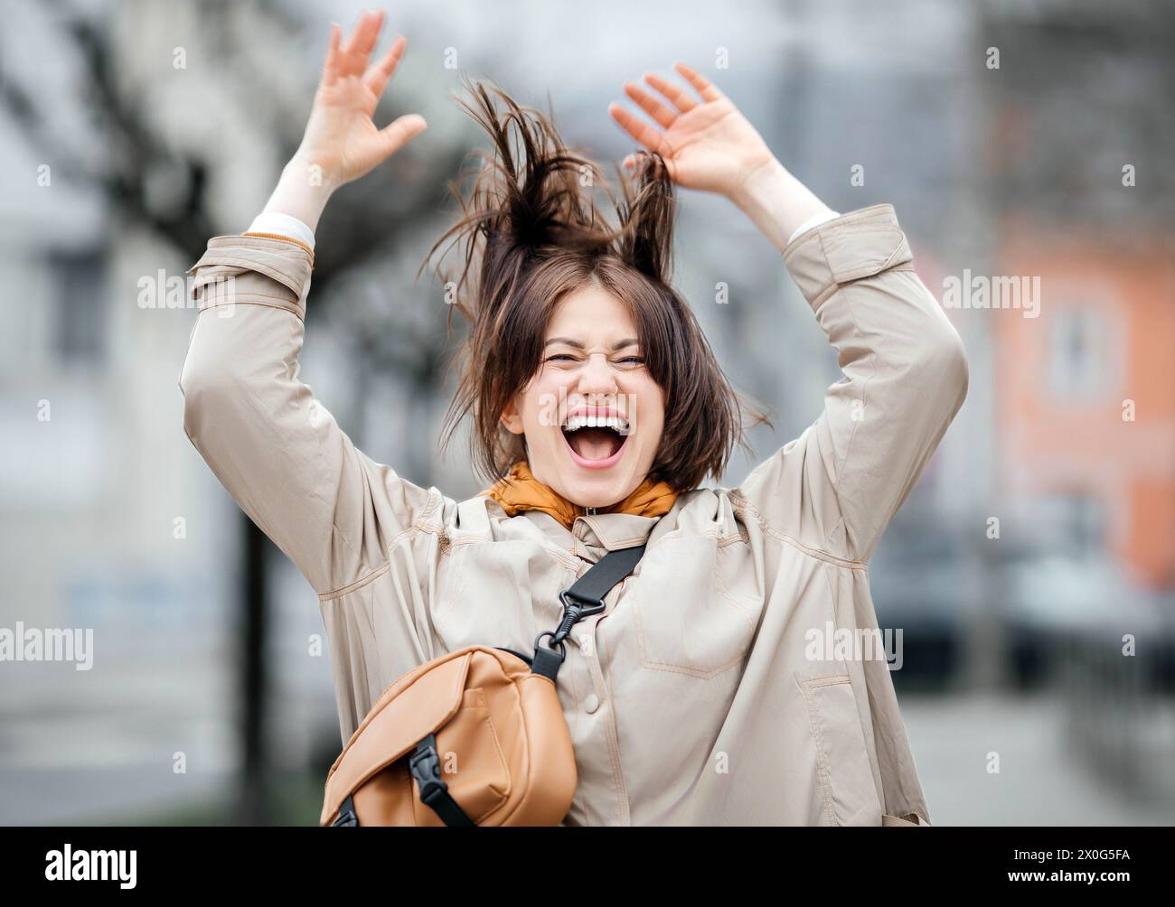 Euphorische Frau mit fröhlichem Ausdruck, Arme hoch, städtischer Hintergrund Stockfoto